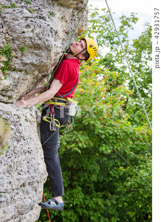 Photo of sportsman in yellow helmet clambering over rock against background of green trees 42931757