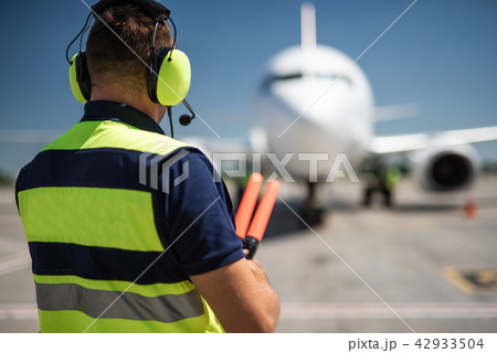 Airport worker in headphones looking at passenger plane 42933504