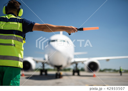 Aviation marshall in headphones directing passenger plane 42933507