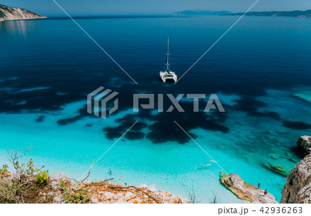 White catamaran yacht at anchor in calm clear azure water lagoon. Unrecognizable tourists relax and White catamaran yacht at anchor in calm clear azure water lagoon. Unrecognizable tourists relax and 42936263