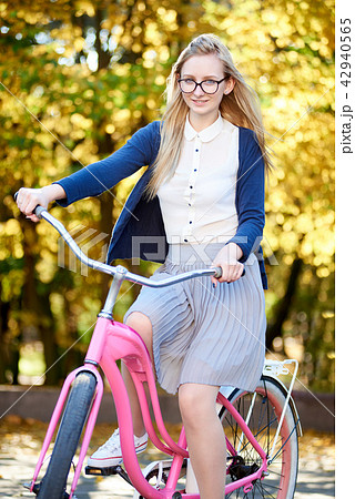 Blond long-haired attractive girl on pink lady bicycle in sunny autumn park on trees background. Blond long-haired attractive girl on pink lady bicycle in sunny autumn park on trees background. 42940565