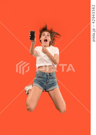 Full length of pretty young woman with mobile phone while jumping Full length of pretty young woman with mobile phone while jumping 42943562