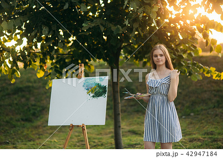 Beautiful girl artist is standing in the park and holding palette with paints Beautiful girl artist is standing in the park and holding palette with paints 42947184