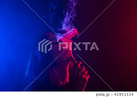 Young woman in neon light and smoke of e-cigarettes or vape on dark background Young woman in neon light and smoke of e-cigarettes or vape on dark background 42951314