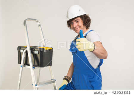 Portrait of handsome builder in white helmet and blue overall showing thumbs up and laughing. Portrait of handsome builder in white helmet and blue overall showing thumbs up and laughing. 42952831