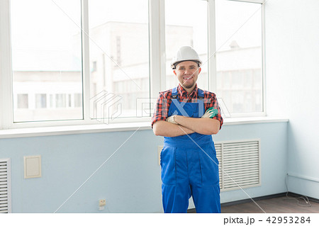 Happy caucasian male builder with crossed hands wearing white helmet in front of window 42953284