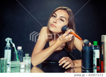 Beauty woman applying makeup. Beautiful girl looking in the mirror and applying cosmetic with a big 42957172