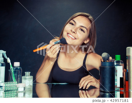 Beauty woman applying makeup. Beautiful girl looking in the mirror and applying cosmetic with a big 42957181