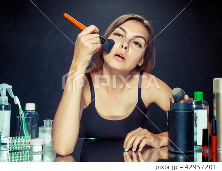 Beauty woman applying makeup. Beautiful girl looking in the mirror and applying cosmetic with a big 42957201