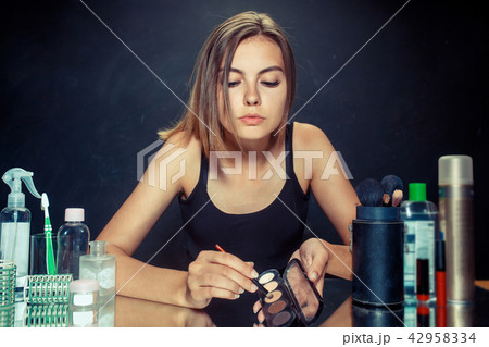 Beauty woman applying makeup. Beautiful girl looking in the mirror and applying cosmetic with a 42958334