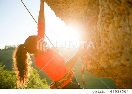Photo of curly-haired female tourist clambering over rock 42958564