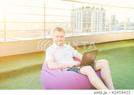 Smiling man sitting on pouf, working on laptop 42959422