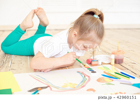 Little blonde girl painting on big white paper while laying on the floor indoors Little blonde girl painting on big white paper while laying on the floor indoors 42960151