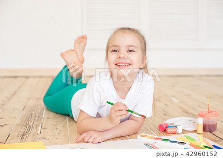 Little blonde girl painting on big white paper while laying on the floor indoors 42960152