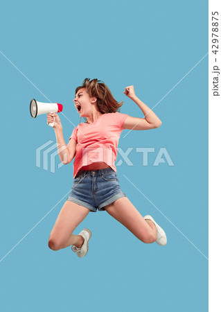 Beautiful young woman jumping with megaphone isolated over blue background 42978875