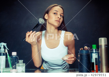 Beauty woman applying makeup. Beautiful girl looking in the mirror and applying cosmetic with a big 42979551