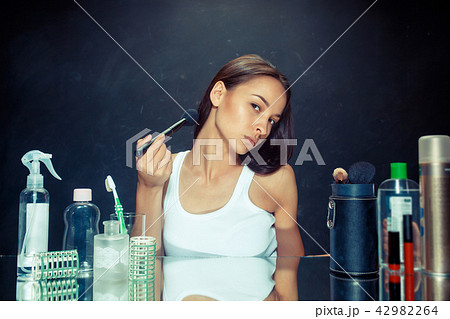 Beauty woman applying makeup. Beautiful girl looking in the mirror and applying cosmetic with a big Beauty woman applying makeup. Beautiful girl looking in the mirror and applying cosmetic with a big 42982264