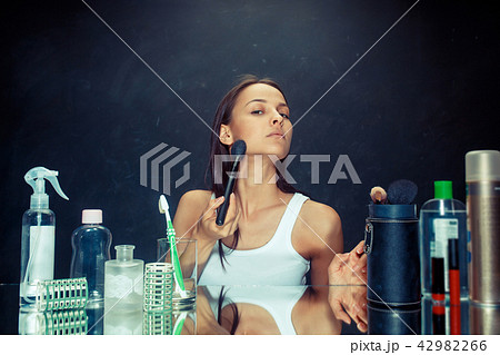 Beauty woman applying makeup. Beautiful girl looking in the mirror and applying cosmetic with a big 42982266