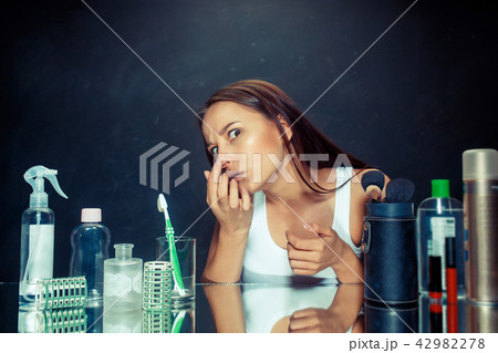 Unsatisfied young woman looking at her self in mirror on black background Unsatisfied young woman looking at her self in mirror on black background 42982278