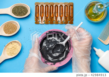 Photo from above with pink cup with black clay, mask oil, wooden spoons, comb, human hands with Photo from above with pink cup with black clay, mask oil, wooden spoons, comb, human hands with 42984913