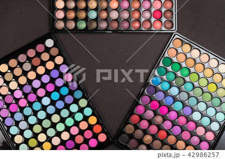 Make-up frame made of colorful eyeshadow palettes arranged as triangle on black 42986257