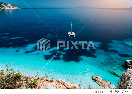 White catamaran yacht at anchor in calm clear azure water lagoon. Unrecognizable tourists relax and 42986778