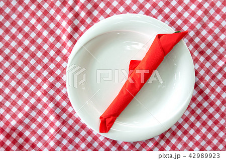 White plate with cutlery wraped in red napkin 42989923