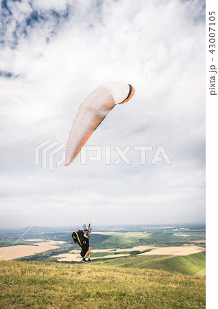 A man paraglider taking off from the edge of the mountain with fields in the background. Paragliding A man paraglider taking off from the edge of the mountain with fields in the background. Paragliding 43007105