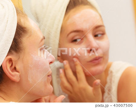 Woman applying mask cream on face in bathroom Woman applying mask cream on face in bathroom 43007500