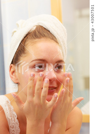 Woman applying mask cream on face in bathroom Woman applying mask cream on face in bathroom 43007501