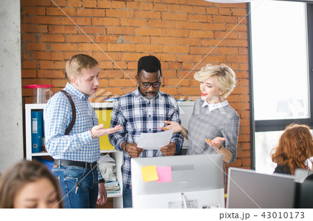 two cooperators with fair hair are setting a task to African guy in glasses holding paper two cooperators with fair hair are setting a task to African guy in glasses holding paper 43010173