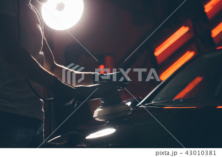 Car detailing - man with orbital polisher in auto repair shop. Selective focus. Car detailing - man with orbital polisher in auto repair shop. Selective focus. 43010381