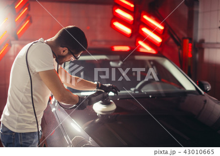 Car detailing - man with orbital polisher in auto repair shop. Selective focus. Car detailing - man with orbital polisher in auto repair shop. Selective focus. 43010665
