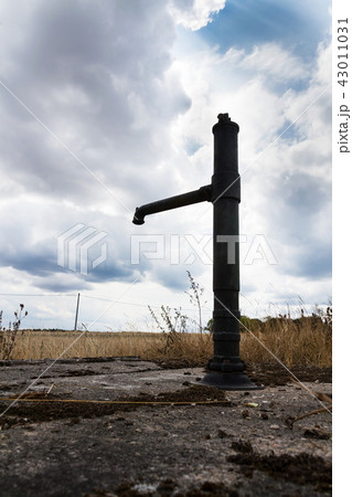 Old pump with dry soil, cloudy sky, water shortage 43011031