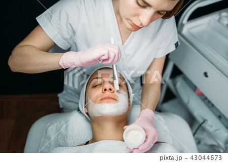 Doctor in gloves rubs the cream on patient face 43044673