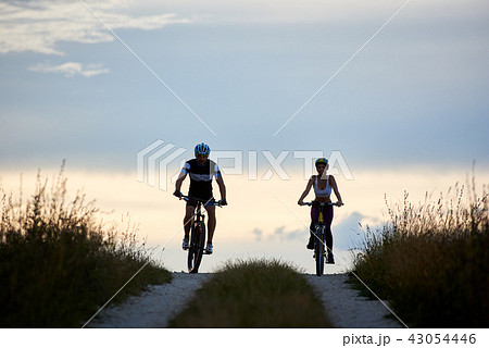 Pair of bicyclist riding bikes on country road. Fit young people in sportswear cycling downhill Pair of bicyclist riding bikes on country road. Fit young people in sportswear cycling downhill 43054446