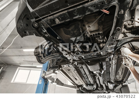 Car mechanic inspecting car wheel and repair suspension detail. Lifted automobile at repair service Car mechanic inspecting car wheel and repair suspension detail. Lifted automobile at repair service 43070522