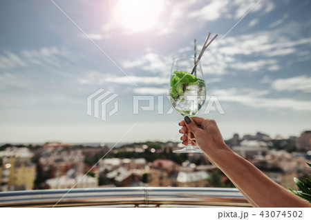 Female hand holding glass of cocktail with drinking straw 43074502
