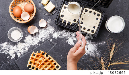Photo on top of flour, eggs, waffle iron, spikelets, fresh roasted waffles, human hands Photo on top of flour, eggs, waffle iron, spikelets, fresh roasted waffles, human hands 43082665