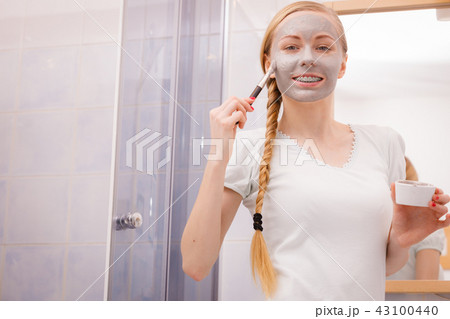 Happy young woman applying mud mask on face Happy young woman applying mud mask on face 43100440