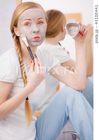 Happy young woman applying mud mask on face Happy young woman applying mud mask on face 43100441