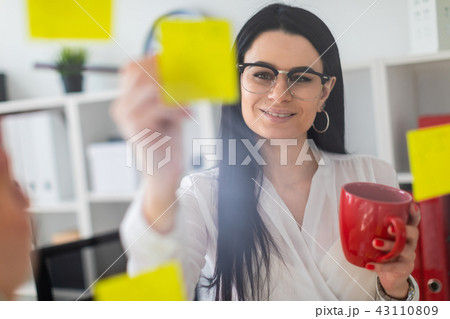 A young girl stands near the board with stickers and holds a red cup and pencil in her hands. A young girl stands near the board with stickers and holds a red cup and pencil in her hands. 43110809