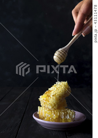 pieces of fresh honeycomb with a wooden dipper dripping honey on a ceramic plate on a slate pieces of fresh honeycomb with a wooden dipper dripping honey on a ceramic plate on a slate 43111478
