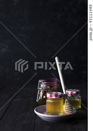 glass jar of honey and stick on a ceramic plate on a dark concrete background , copy space 43111489