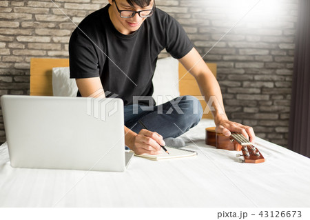 Happy young asian man playing ukulele sitting on bed in bedroom. Happy young asian man playing ukulele sitting on bed in bedroom. 43126673