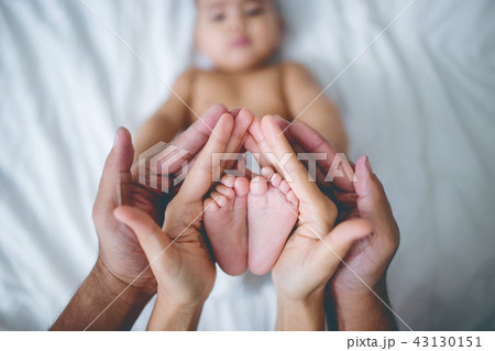 Hands of parents holds baby feet on the bed. 43130151