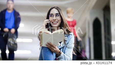 The girl is waiting for the subway train stop, reading the book and speaking the phone 43141174