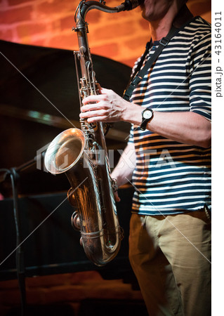 An anonymous musician in a striped t-shirt plays the saxophone in a jazz bar, live performance 43164011