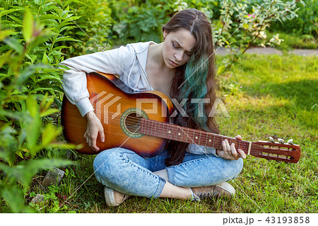 Young woman sitting in grass and playing guitar 43193858