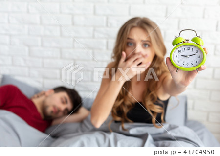 Late at work. Shocked girl holding alarm clock in bed Late at work. Shocked girl holding alarm clock in bed 43204950